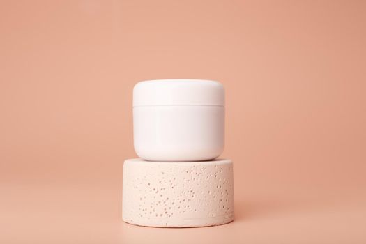 White cosmetic jar on gypsum podium against pastel beige background with copy space. Concept of organic natural skin care products with nourishing, moisturizing or anti aging effect