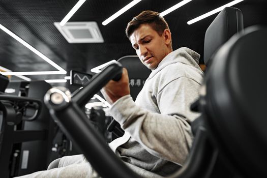 Young fit bodybuilder man doing arms workout training in the gym on machine, close up