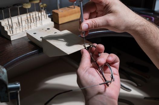 Optical technician fixing glasses. Close-up of male hands with screwdriver and goggles frame