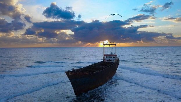 Aerial view of the sea and ship aground. Cargo vessel Demetrios II shipwrecked near rocky coast in Mediterranean sea at Paphos, Cyprus. Beautiful sunset and clouds over the sea.