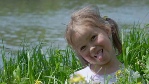 Portrait of a smiling little girl. Baby girl sitting in tall grass. Tiny kid have fun, enjoy nature outdoors.