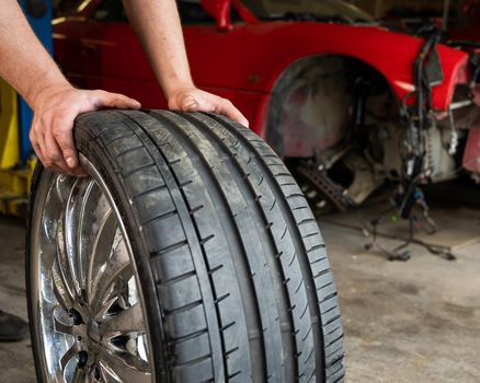 An auto mechanic holds a wheel of a car. Change of car tires according to the season.
