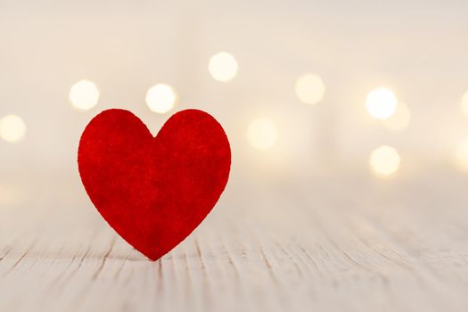 on a light wooden background a red heart, in the background the garland is out of focus