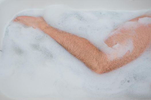 Funny picture of a man taking a relaxing bath. Close-up of male feet in a bubble bath. Top view.