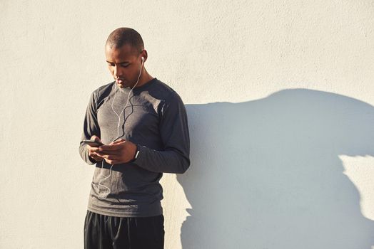 Little break. Close up portrait of motivated africanathlete taking a break and listening music on earphones while standing against the white wall. Cardio training. Morning workout. Sport motivation concept. Fitness