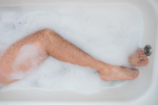 Funny picture of a man taking a relaxing bath. Close-up of male feet in a bubble bath. Top view.