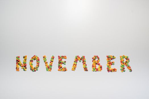 The inscription November on a white background. Confectionery sprinkles in the form of multi-colored maple leaves. Copy space