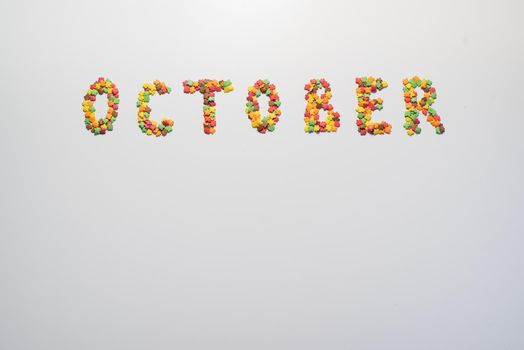 October inscription on a white background. Confectionery sprinkles in the form of multi-colored maple leaves.
