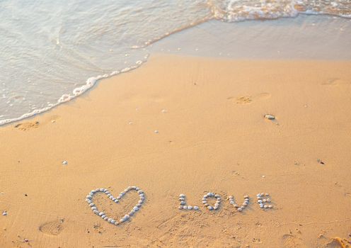 On the sand shells lined with heart and the word love.