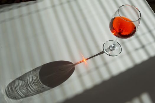 A glass of red wine on a white table with a shade from the blinds.