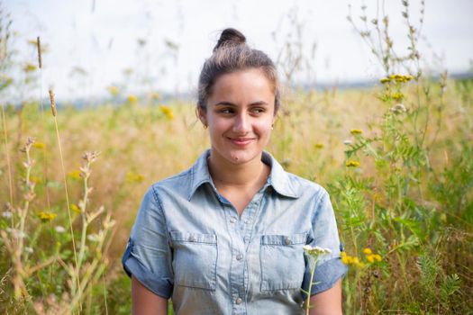 beautiful young woman sits in a meadow in flowers on a sunny summer day and smiles.