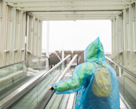A woman in a raincoat rises on an escalator. Girl in protective clothing from the rain. Back view