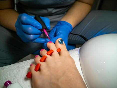a gloved master makes a pedicure for a client. close-up no face. woman in a nail salon paints her nails with red varnish