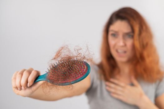 Caucasian woman with a grimace of horror holds a massage comb with a bun of hair. Hair loss and female pattern baldness