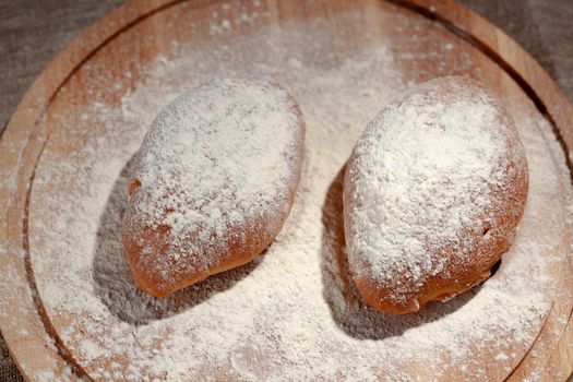 two patties in flour on a round chopping board, homemade pastries