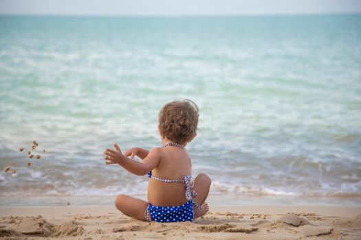 cute toddler girl in blue swimsuit playing in the sand on the ocean beach. back view