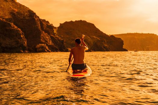 Side view foto of a man swiming and relaxing on the sup board. Sportive man in the sea on the Stand Up Paddle Board SUP. The concept of an active and healthy life in harmony with nature