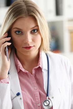 Beautiful female blond doctor talking on phone at the office woman discussing the disease and giving online consultation remote training education