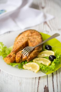 piece of fried salmon fish in a plate with lemon and herbs