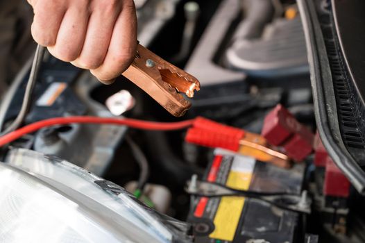 The mechanic connects the clamps to the discharged car battery