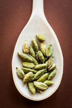 Whole cardamom in wooden spoon on brown background