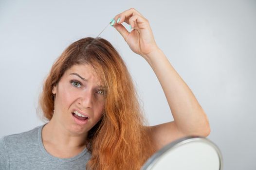 Caucasian woman finds gray hair and removes it with tweezers. Signs of aging
