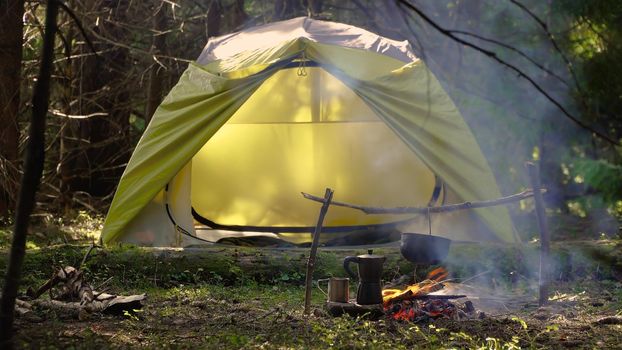 Camp in a beautiful forest. A kettle over the fire near the green tent. Travel concept