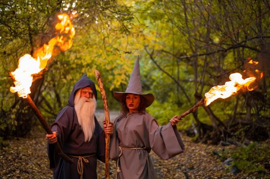 Wizard and sorceress in the autumn forest. Elderly man and woman in carnival costumes for halloween.