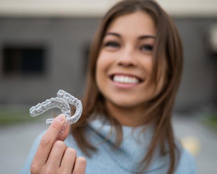 Caucasian woman with white smile holding transparent removable retainer. Bite correction device