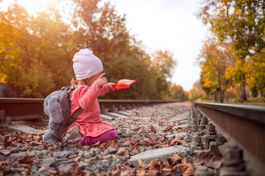 adorable toddler girl playing with a scoop on the railroad in sunshine