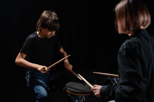 Young caucasian woman teaches a boy to play the drums in the studio on a black background. Music school student.