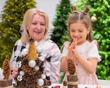 Elderly caucasian woman making pine cones decoration for christmas with two granddaughters.