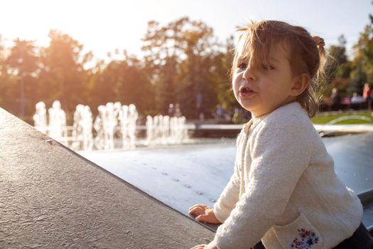 adorable toddler girl makes faces and grimaces against the backdrop of the park. the child plays cheerfully. happy childhood