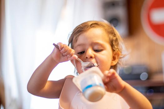 cute baby eating yogurt with spoon by himself. adorable toddler has lunch. hungry child eas food