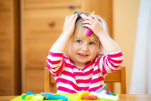 Smiling girl playing with plasticine at home