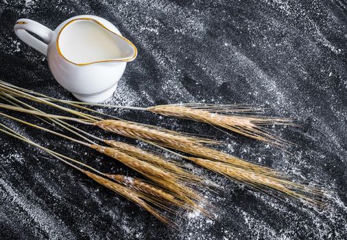 milk jug and ears of wheat on a black textured table