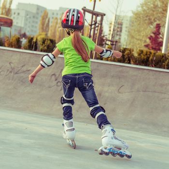 Back view of little girl in helmet on roller-skates in park