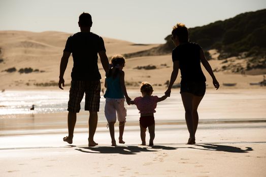 Silhouette of family, two adults and a child at the coast in sunset