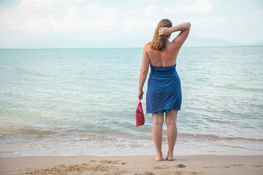 a woman holds in her hand a mesh shopping bag and stands on the edge of the sea on a sandy beach. ecology concept. conscious consumption