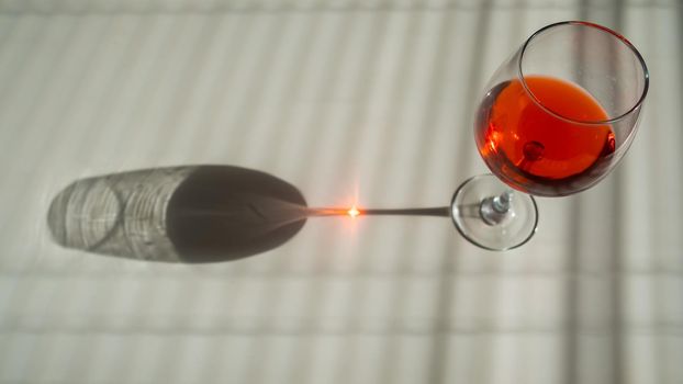 A glass of red wine on a white table with a shade from the blinds.