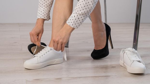 Close-up business woman takes off her shoes puts on white leather sneakers