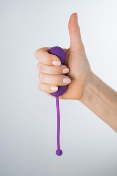 A woman recommends an electronic Kegel trainer for training pelvic floor muscles on a white background. Thumb up.