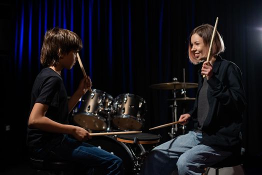 Young caucasian woman teaches a boy to play the drums in the studio on a black background. Music school student.