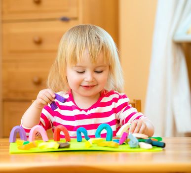 Smiling girl playing with plasticine at home