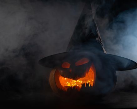 A creepy pumpkin with a carved grimace in the smoke. Jack o lantern in the dark