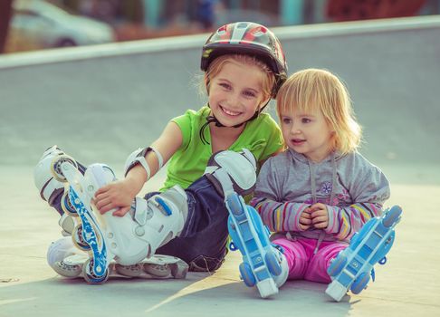 two beautiful little sisters in a roller skates sitting on the street
