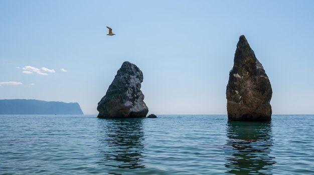 Summer sea landscape with clear sky and volcanic rocky coastline. Calm clear sea, small waves on the empty pebbles beach in rocky lagoon, volcanic basalt as in Iceland. Never-ending beauty of nature