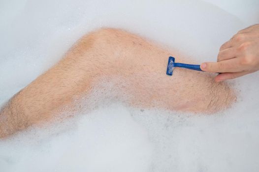 Funny picture of a man taking a relaxing bath and shaving his legs. Close-up of male feet in a bubble bath. Top view