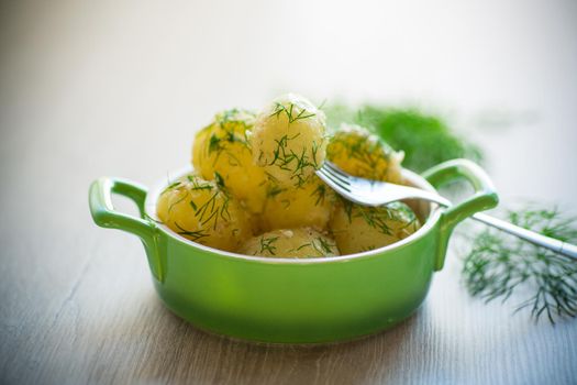 boiled early potatoes with butter and fresh dill in a bowl on a wooden table