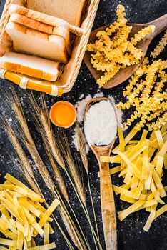 uncooked pasta, bread and other products on a black textured table